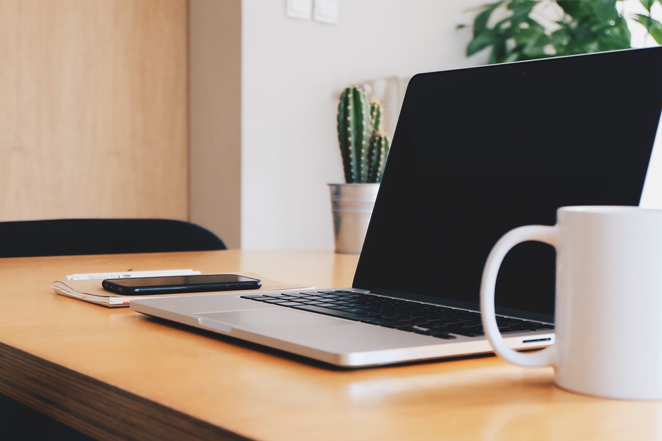 Laptop auf einem Tisch neben Tasse und Handy