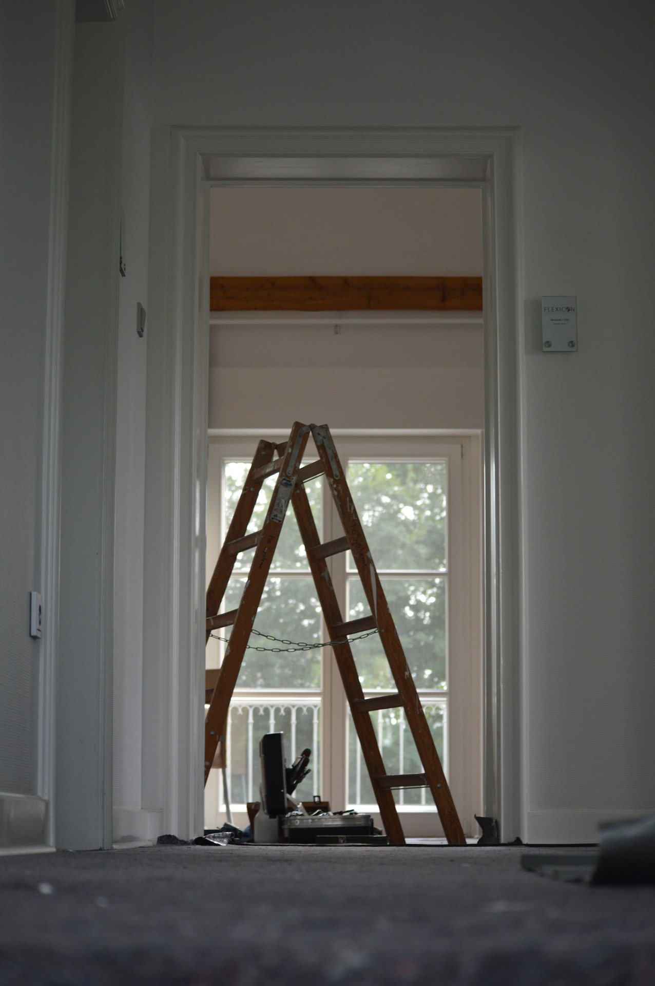 Leiter bei Malerarbeiten im Haus. Blickwinkel aus anderem Zimmer, bei dem die Zimmertüre ausgehängt ist.