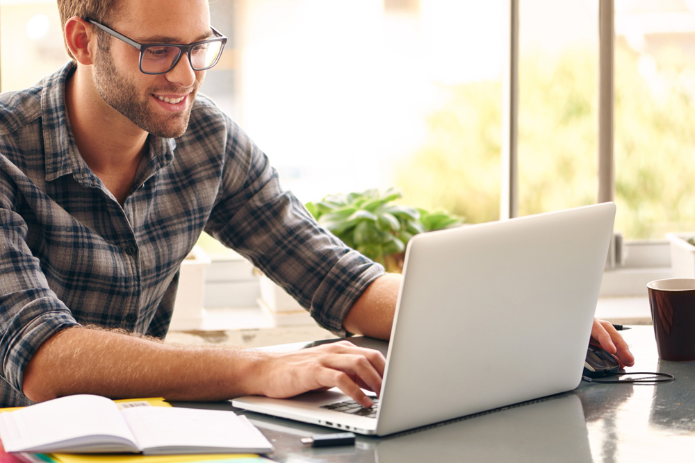 Mann mit Brille und Hemd sitzt an einem weißten Laptop 