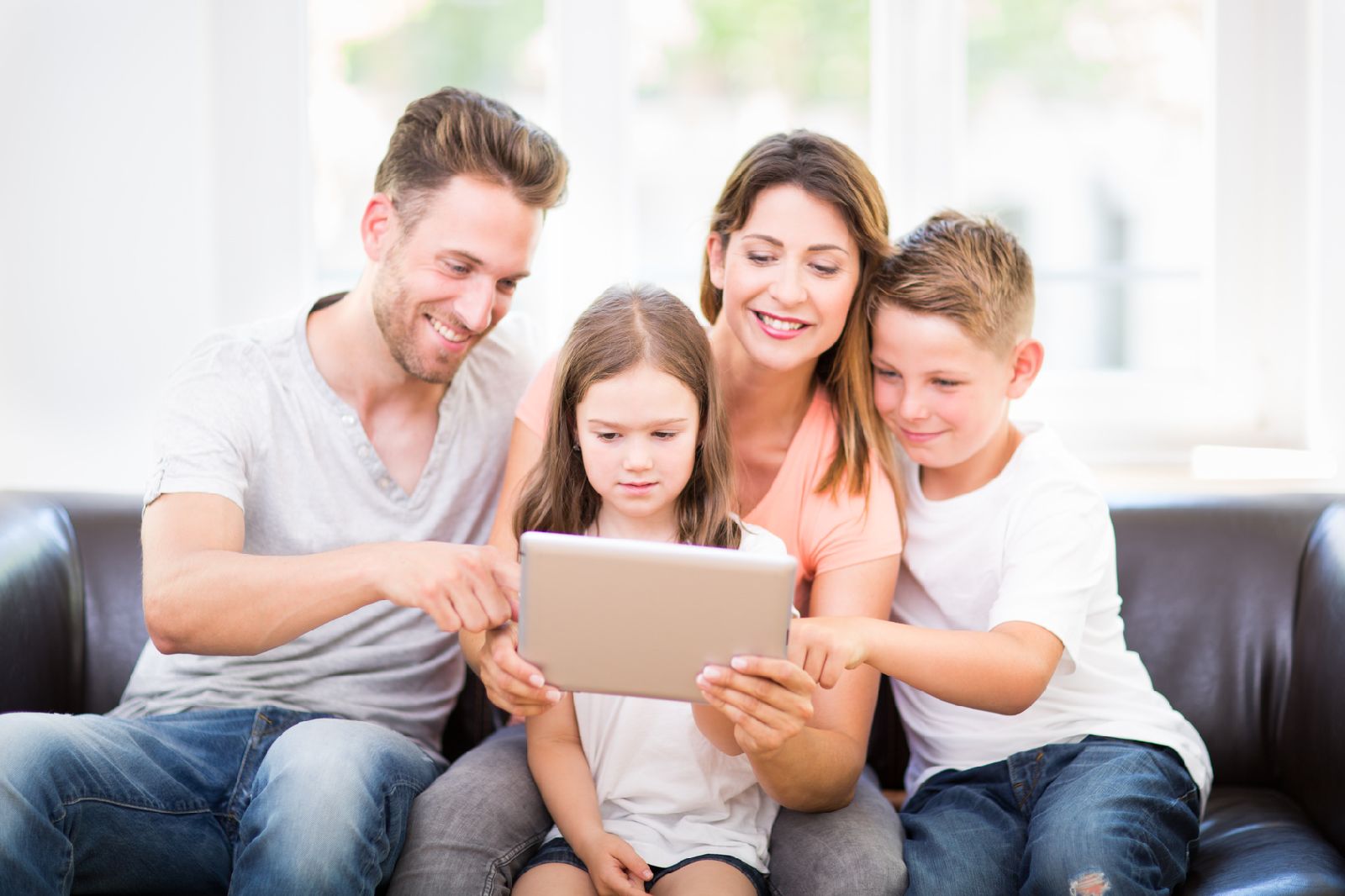 Familie sitzt auf einem schwarzen Sofa mit einem Tablet 