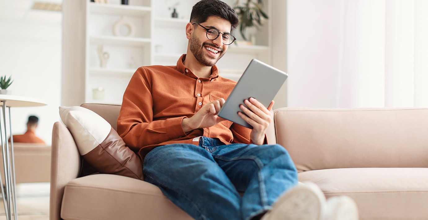 Ein lächelnder Kunde auf dem Sofa zu Hause mit einem Tablet in der Hand