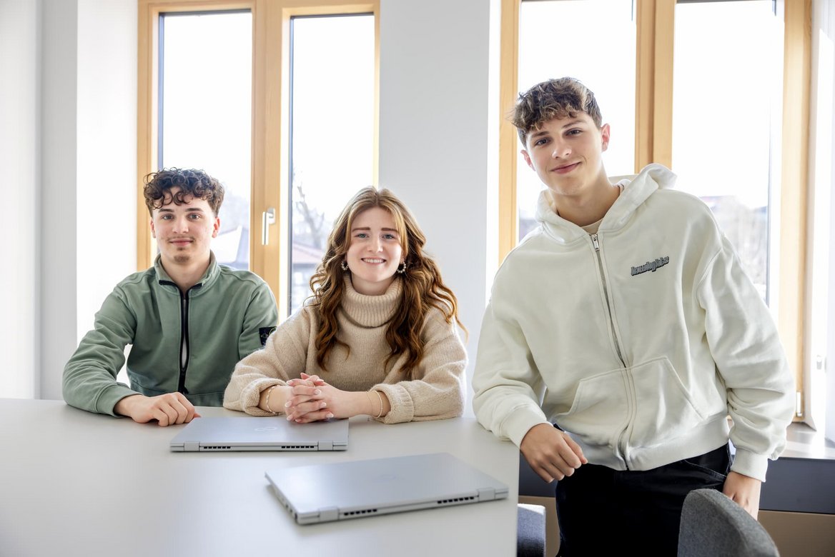 Drei Auszubildende in einem Besprechungsraum mit Laptops an einem Tisch.