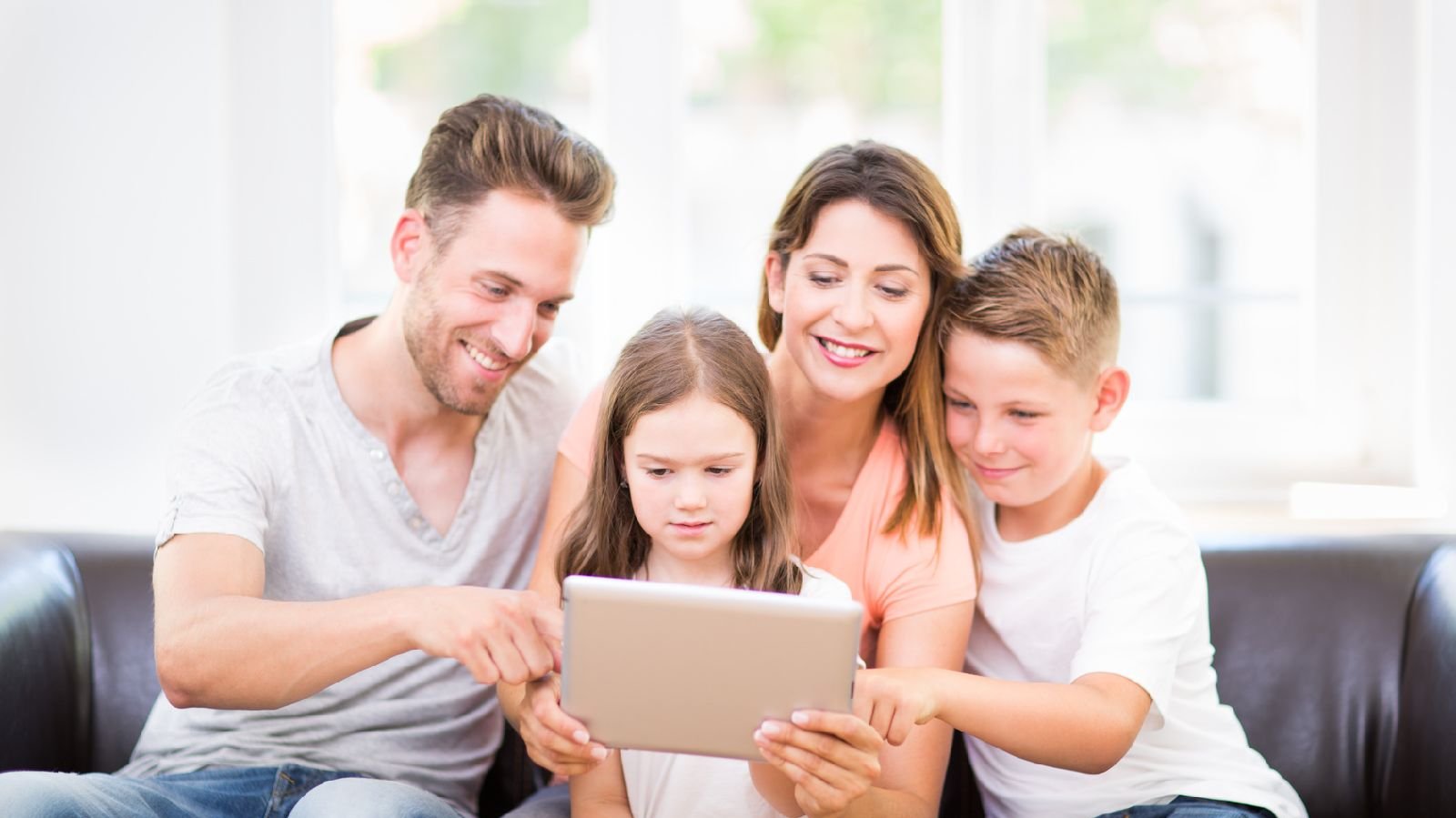 Familie sitzt auf dem Sofa und hat ein Tablet in der Hand.