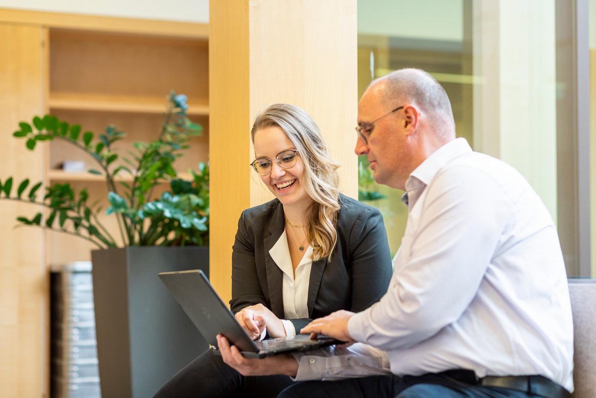 Zwei Mitarbeitende schauen auf einen Laptop und unterhalten sich.